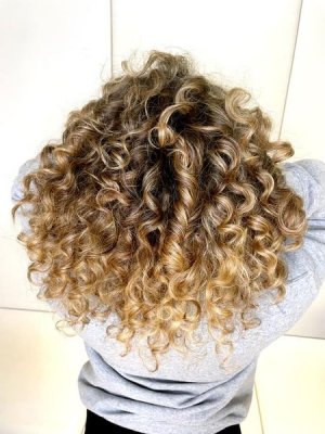 Curl with bouncy blonde curls in a grey top with white background at the klinik salon London 