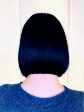 A girl with a blue top and black hair standing with her back to the camera at the klinik salon showing off her bob.
